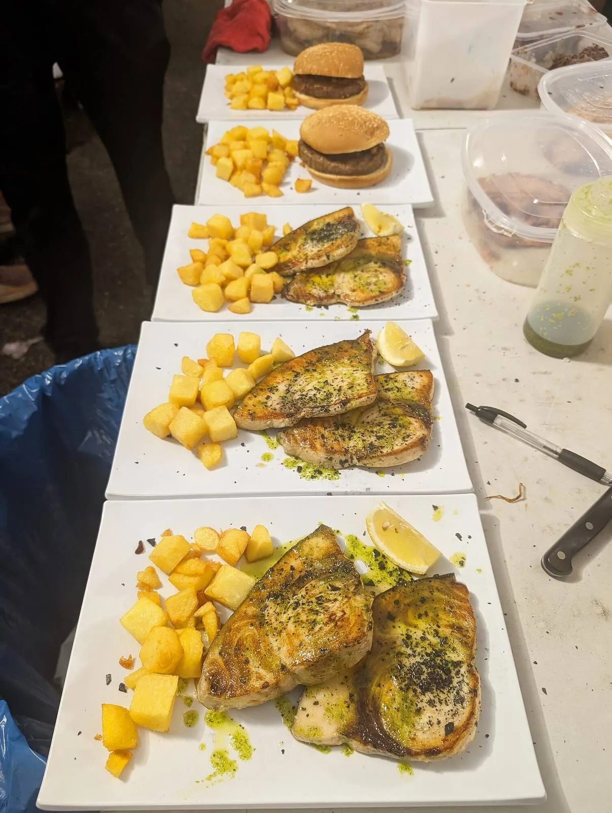 Platos de pescado y guarnición alineados en una mesa de trabajo